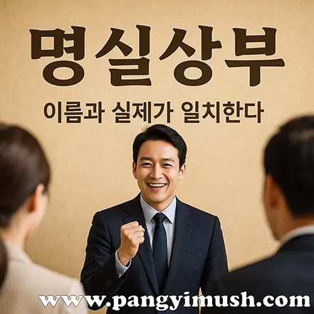 명실상부 뜻을 설명하는 장면으로, 정장을 입은 남성이 미소를 지으며 주먹을 쥐고 사람들 앞에서 이야기하는 모습이 담긴 이미지